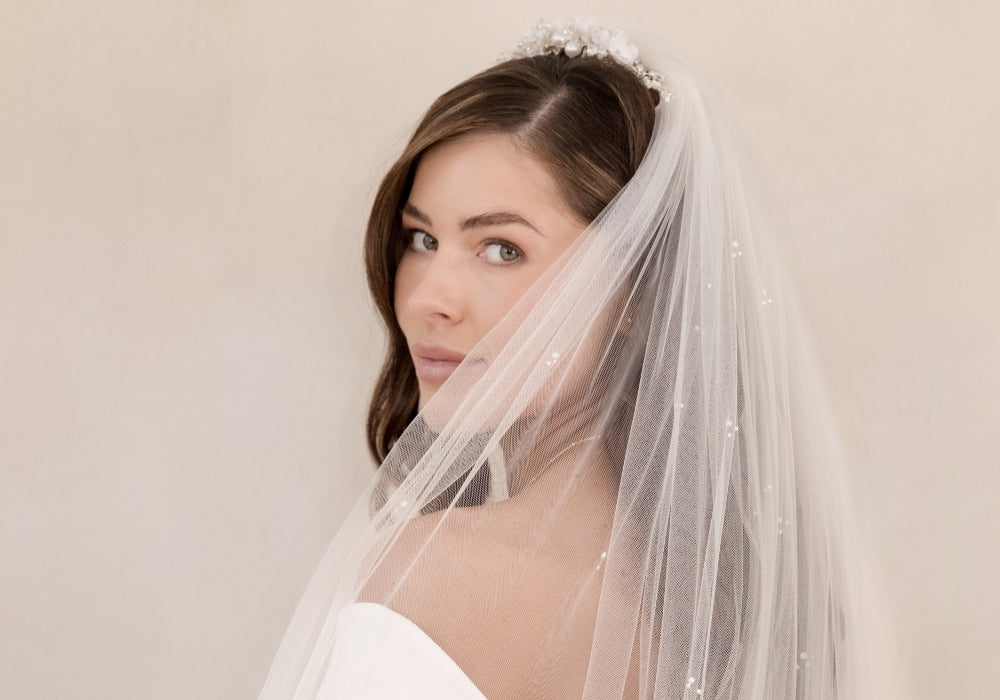 Women bride wearing a wedding comb and plain white bridal veil across her face, against a plain background. 