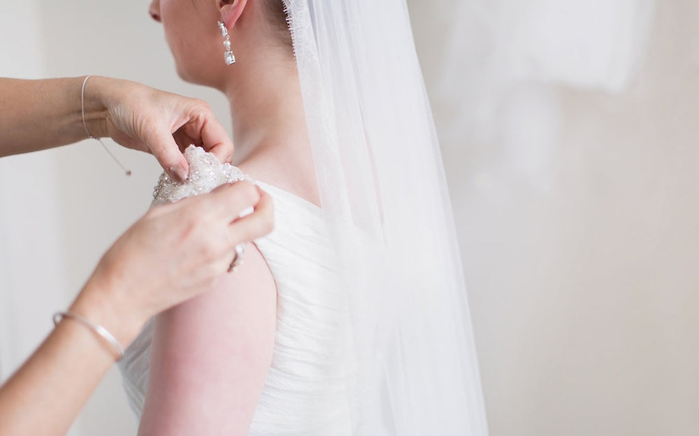 Person adjusting a white lace garment on a bride, likely preparing for a wedding.