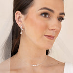 Woman wearing pearl earrings and a delicate necklace with a neutral background