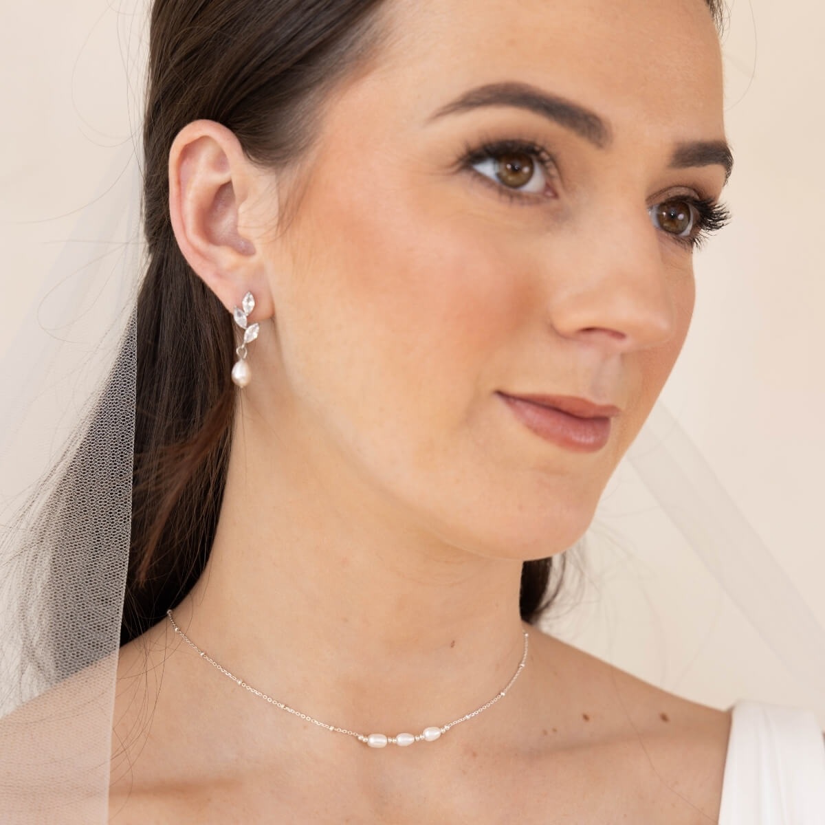 Woman wearing pearl earrings and a delicate necklace with a neutral background