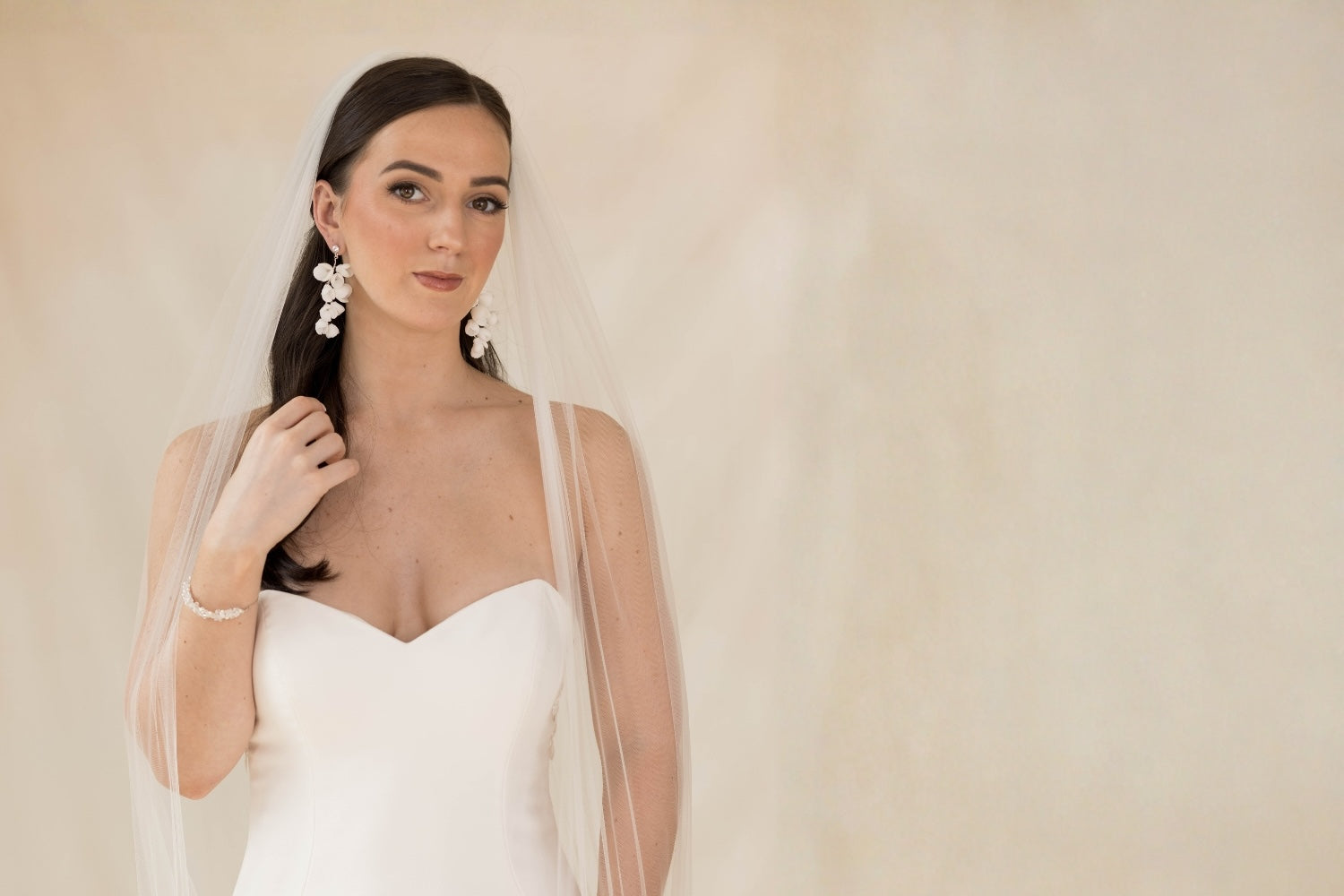 Woman wearing a white wedding dress with a veil against a plain background